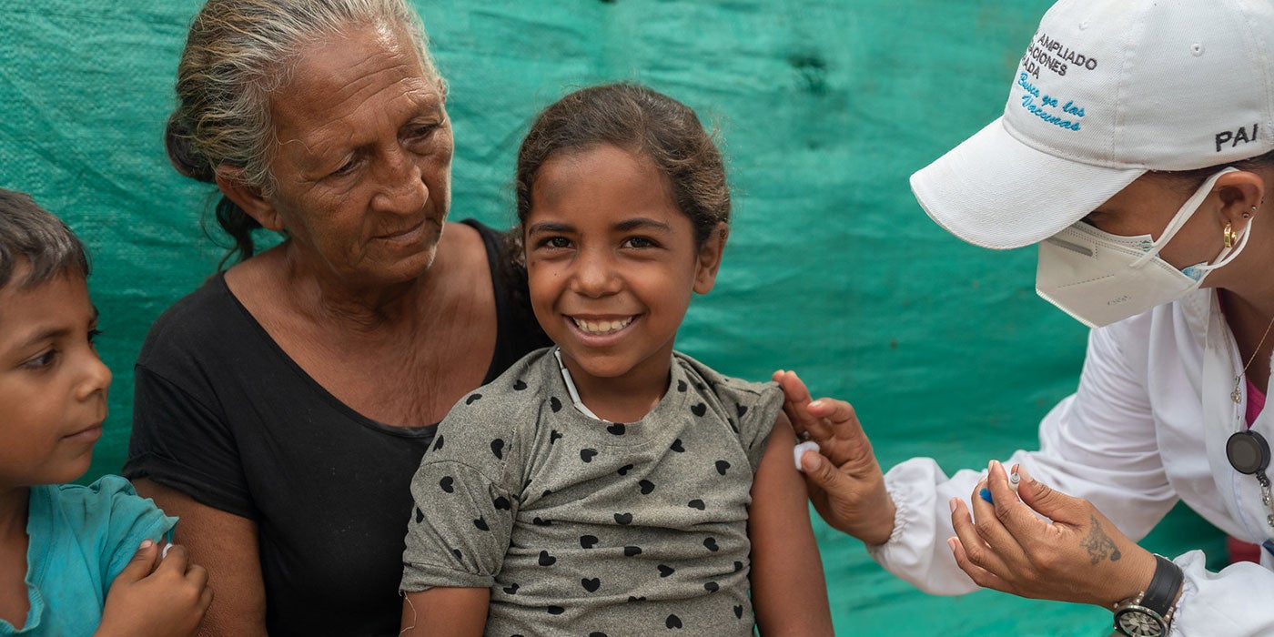 Menina recebe vacinas de profissional de saúde
