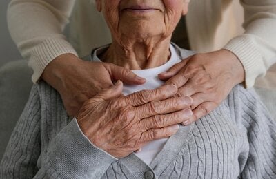 Mujer irreconocible que expresa su cuidado hacia una anciana, abrazándola desde atrás con las manos en la mano. Dos mujeres adultas de diferente edad.