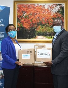 Dr Eldonna Boisson, PAHO-WHO Representative and Minister Renward Wells, Minister of Health hold donations of COVID-19 test kits 