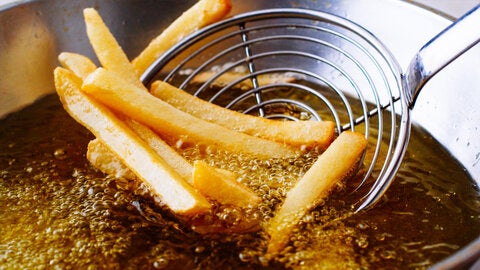 French fries being deep fried in oil and scooped with a ladle 