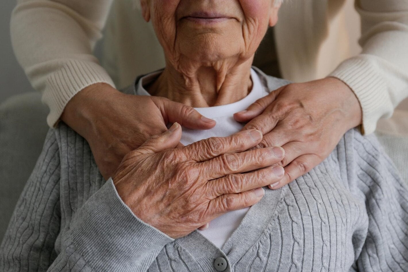 Mujer irreconocible que expresa su cuidado hacia una anciana, abrazándola desde atrás con las manos en la mano. Dos mujeres adultas de diferente edad.