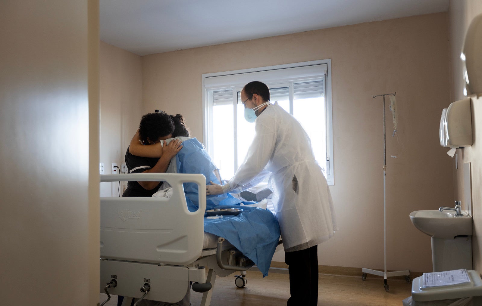 A patient hugs a family member, while a doctor waits at the side of the hospital bed.