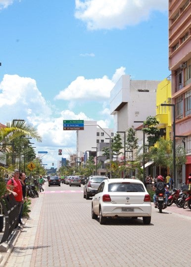 Escena urbana de Campo Grande, con vehículos y una moto circulando por la calzada y dos peatones en la acera en la izquierda