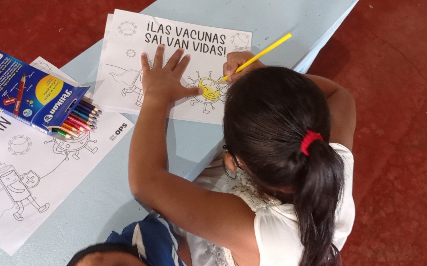 Niña coloreando una hoja con el mensaje "Las vacunas salvan vidas"