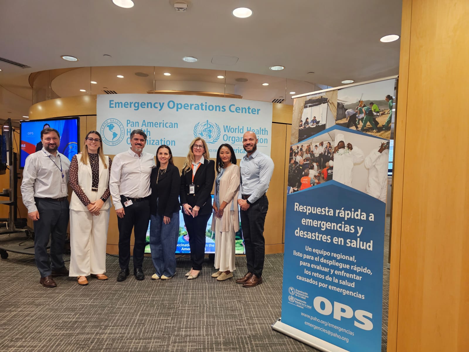 Delegación de salud de São Paulo y equipo de la OPS/OMS posan en el Centro de Operaciones de Emergencia, junto a un banner sobre respuesta a emergencias sanitarias.