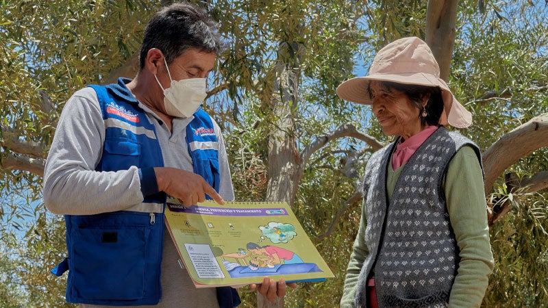Mujer adulta mayor recibiendo información sobre vacunas en un entorno rural
