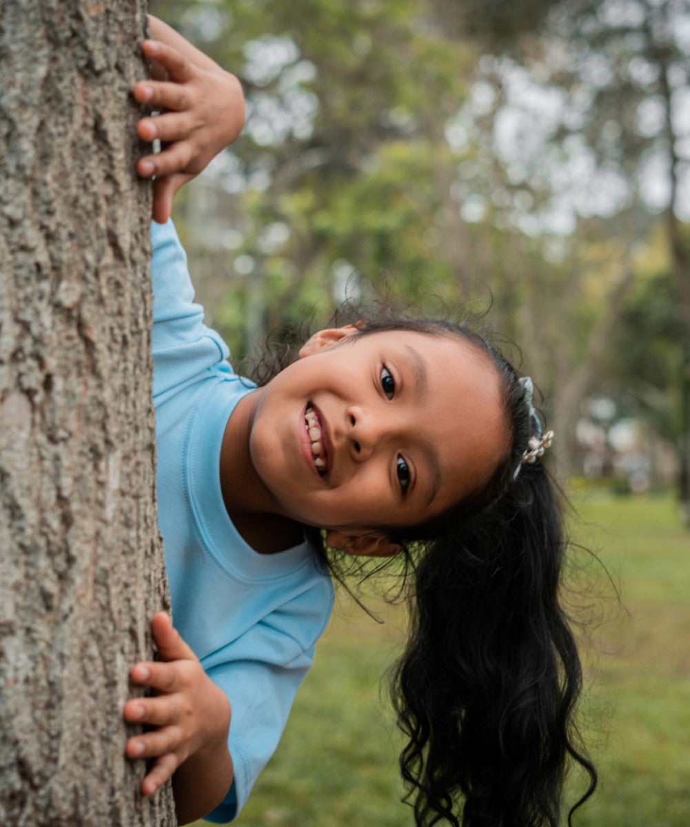 girl peerking around a tree trunk