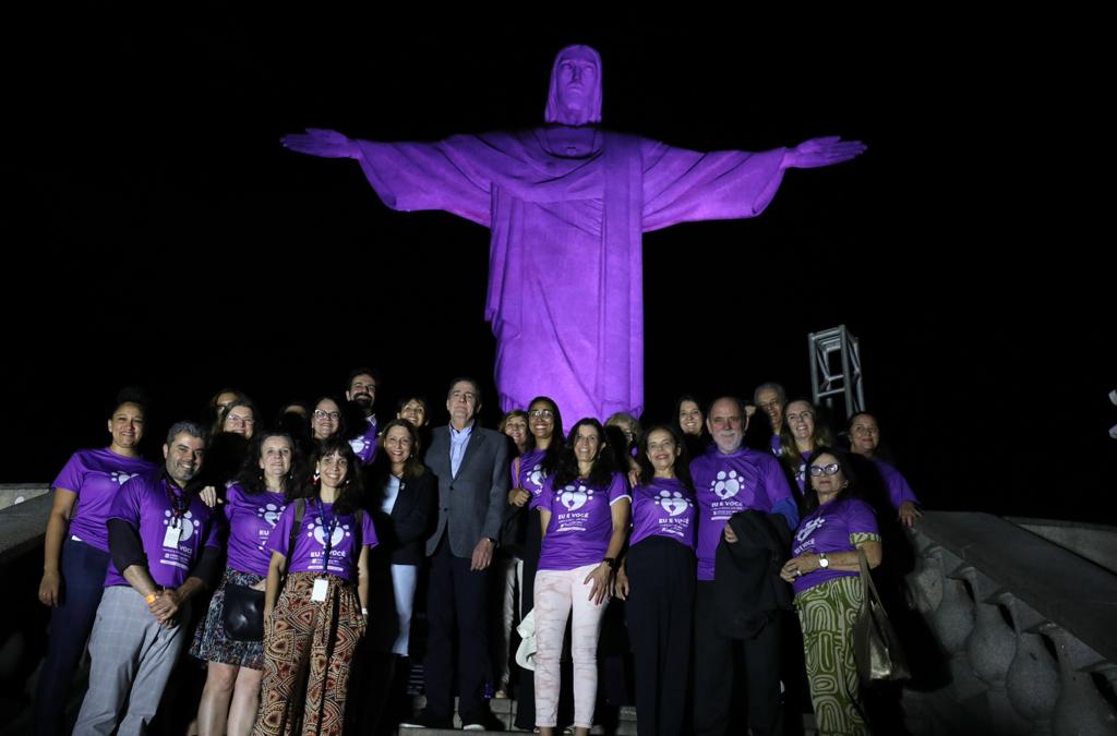 Cristo redentor iluminado de roxo, com pessoas na frente