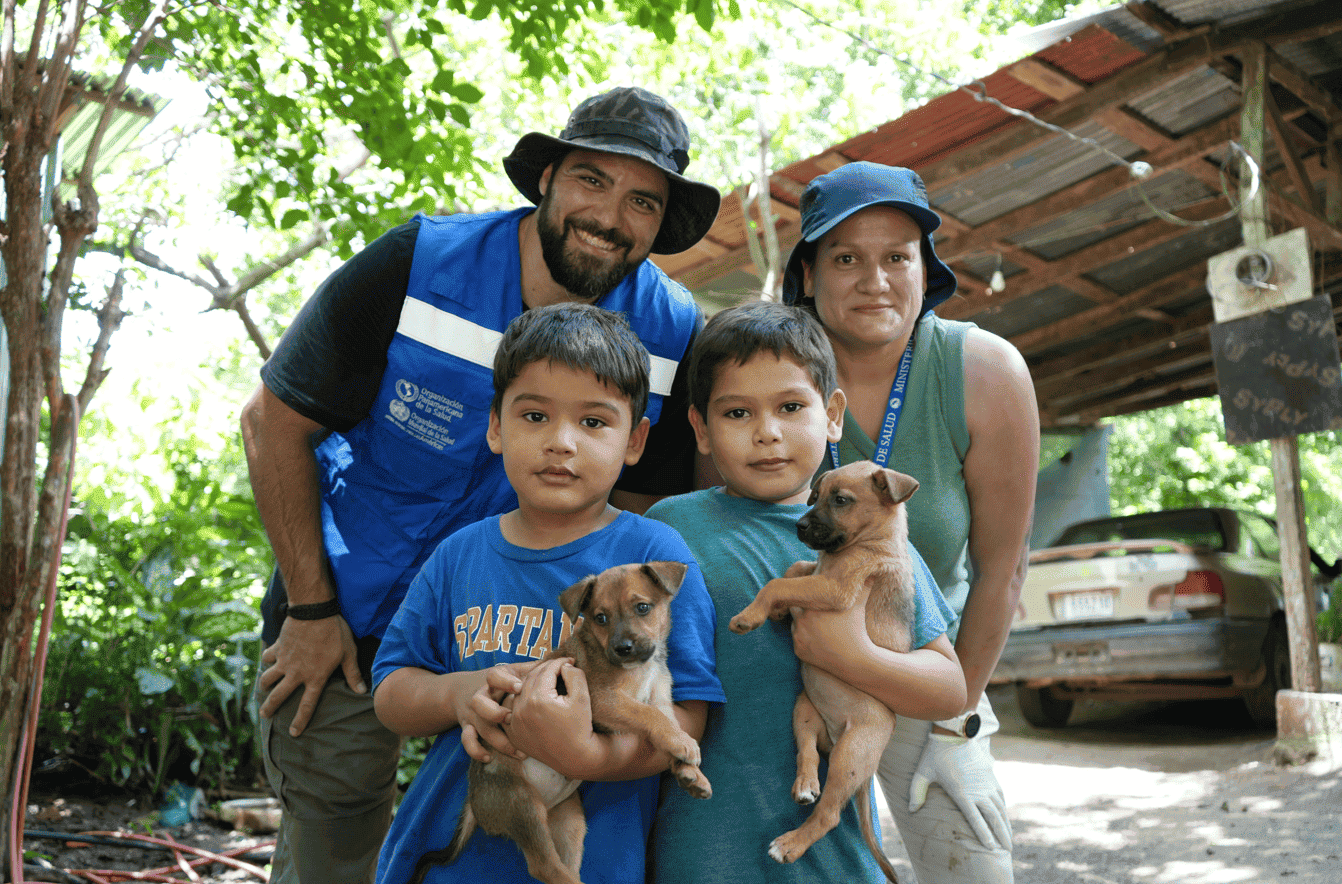 Personal de OPS y Ministerio de Salud posan para la fotografía con 2 niños de la comunidad y sus mascotas