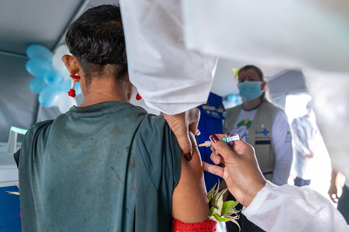 Health worker vaccinates indigenous person, closely followed by the Ministry of Health and PAHO teams.