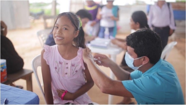 Adolescent girl in pink smiles at the camera as she receives vaccine in Ucayaliu, Peru