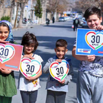 Foto de cuatro niños en medio de una calle sin tráfico sosteniendo carteles con el dibujo de un 30 dentro de la silueta de un corazón