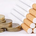 Fotografía de unas monedas apiladas junto a un grupo de cigarrillos amontonados en pirámide
