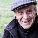 Fotografía de un hombre de edad avanzada, sonriendo, ataviado con una gorra a cuadros y una chamarra oscura