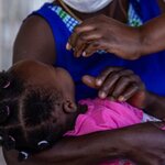 Child held by mother receives oral vaccine