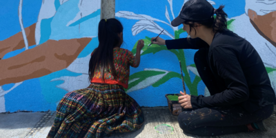 Niña y artista pintan mural