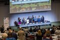 Conference room at COP11 meeting; panelists stand and applaud at the front, audience members also standing and clapping.