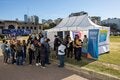 Un grupo de personas espera frente a un gazebo blanco, con banderas y banners de OPS, para aplicarse sus vacunas en la Feria del Libro.