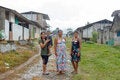 Tres mujeres y un niño posan en una calle de una comunidad amazónica rural, rodeados de viviendas de madera y áreas verdes en un día lluvioso.