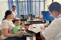Persona adulta con niño pequeño en brazos durante una consulta en un centro de salud, mientras personal sanitario atiende y registra información en una computadora.