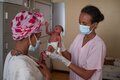 doctor with mask holding newborn baby in clinic in front of its mother