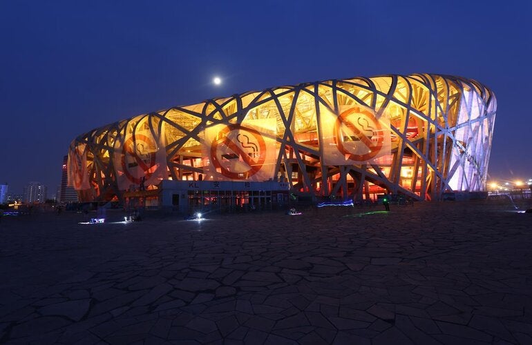 Photo of a big building shaped as a elipse, with no walls, shape made of the bent beams. In the exterior, four large banners with the icon of prohibited smoking