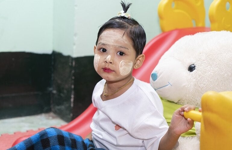 Photo of a young girl with her face painted and seated next to a giant stuffed rabitt