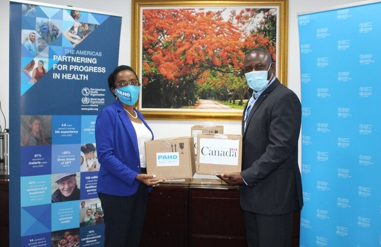 Dr Eldonna Boisson, PAHO-WHO Representative and Minister Renward Wells, Minister of Health hold donations of COVID-19 test kits 