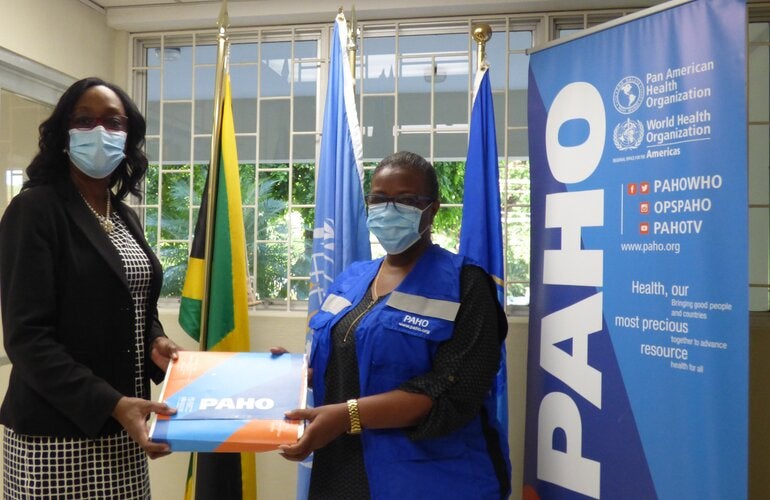 Dr. Michelle Hamilton, Director of the National Public Health Laboratory (left) receives the donation of 6000 Polymerase Chain Reaction (PCR) tests to identify Variants of Concern of COVID-19 (VoC) from Dr. Audrey Morris, Decentralized Regional Advisor, Food and Nutrition (right) at the offices of the Pan American Health Organization/ World Health Organization in Kingston.