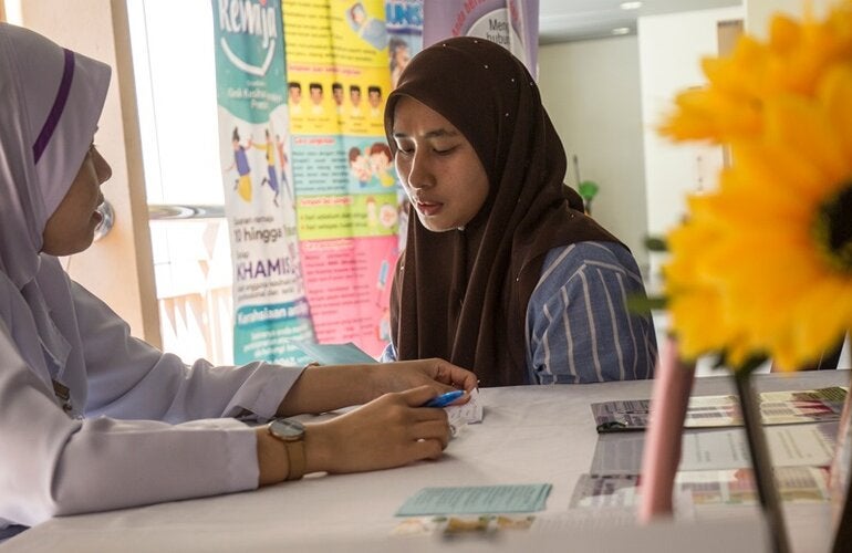 Photo of two women in health care facility; one is the patient, the other the health provider. Both have their heads covered with a scarf 