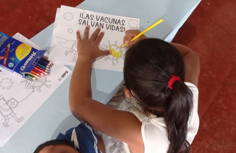 Niña coloreando una hoja con el mensaje "Las vacunas salvan vidas"