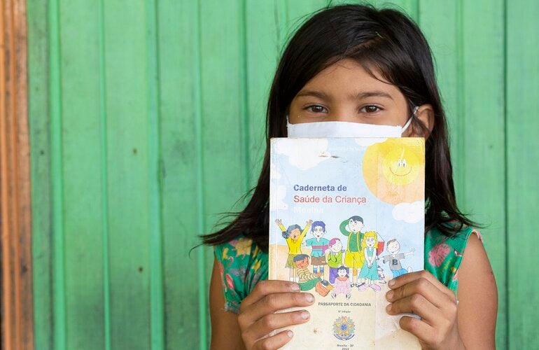 Criança segurando cartão de vacinação, no Brasil
