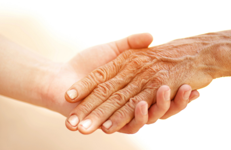 Una mano de persona joven sosteniendo la mano de una persona mayor