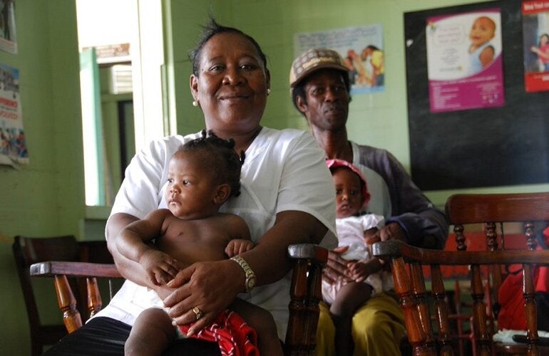 Mujer sentada con bebé y, más atrás, hombre con bebé
