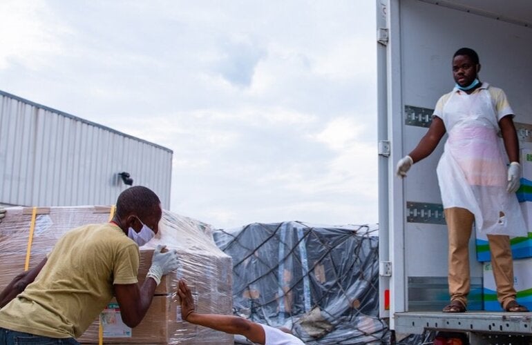 Photo of a group of workers pulling up a load of medicines marked with WHO logo into a truck