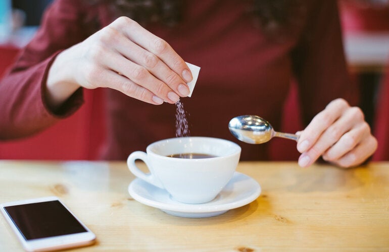 Person adding sugar to beverage. Avoid non-sugar sweeteners