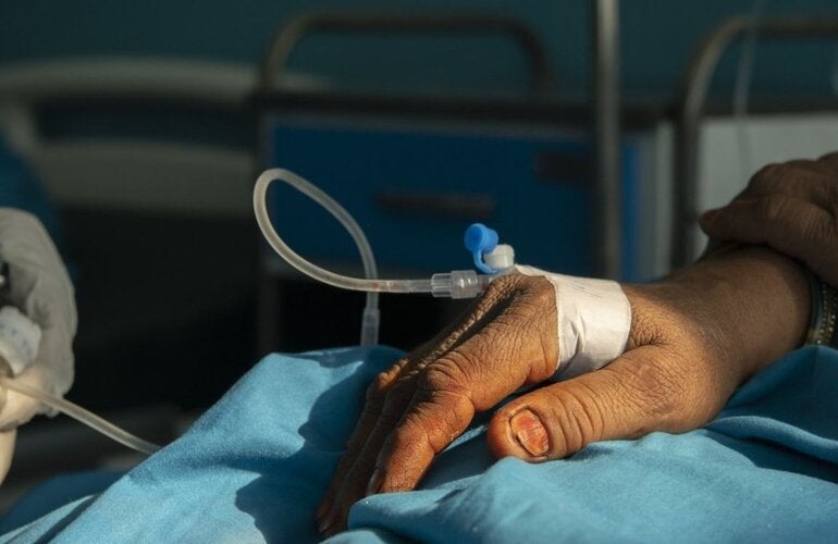 photo of a hand of a patient with an IV and two hands of a health worker adjusting it