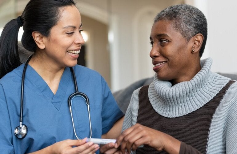 A senior African American female is being helped by her Hispanic female nurse during a home visit. They are listening to each other speak. She is showing her how to use an insulin pen.