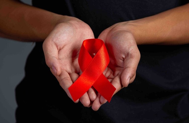 Manos sosteniendo listón rojo refernte al VIH/SIDA