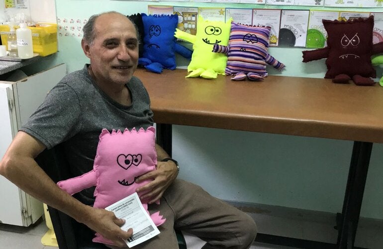Foto de un hombre que acaba de recibir la vacuna y tiene entre sus brazos el muñeco de la alegría que expresa su sentimiento en torno a la vacunación