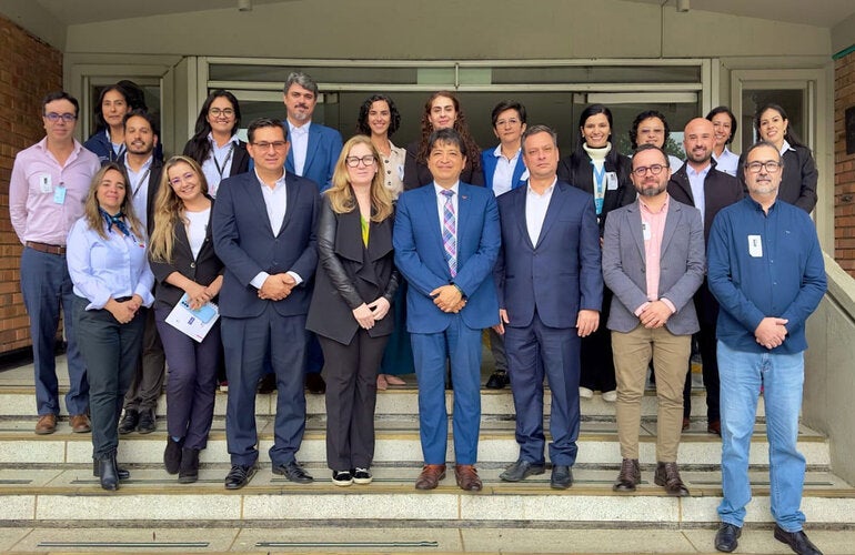 Participantes del evento (hombres y mujeres) con ropa ejecutiva, posan en las escaleras de la entrada de un edificio.
