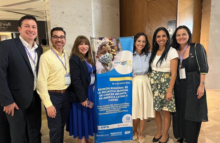 Fotografía de varias personas junto al banner que anuncia la reunión regional de CureAll Americas