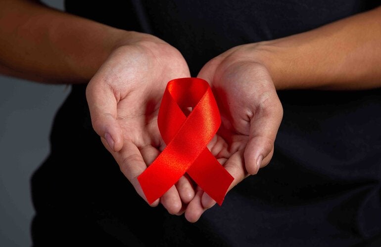Manos sosteniendo listón rojo refernte al VIH/SIDA