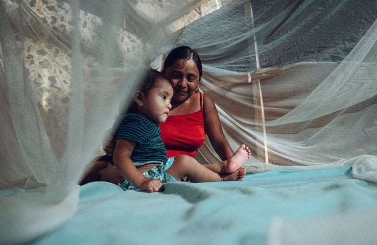 Mother and child under mosquito net over bed