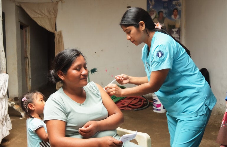 Personal de salud aplica la vacuna a una mujer junto a su hija pequeña