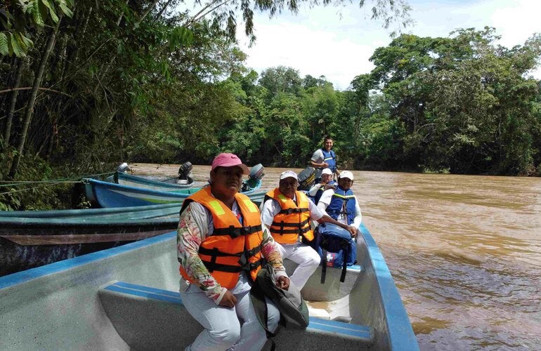 Personas en un bote de madera en la orilla de un río. Las personas tienen chalecos salvavidas.