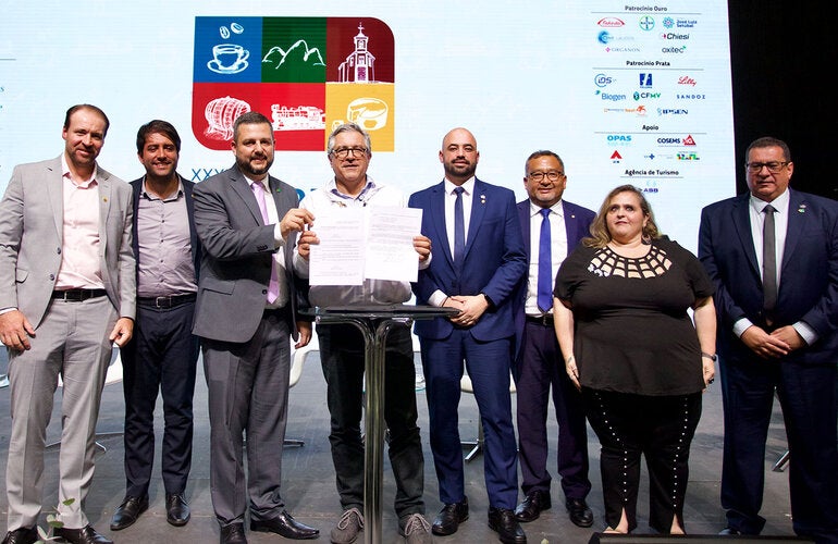 O Ministro da Saúde do Brasil, Alexandre Padilha, segura documentos assinados por ele. Na foto, ao lado dele estão o presidente do Conasems e outras autoridades.