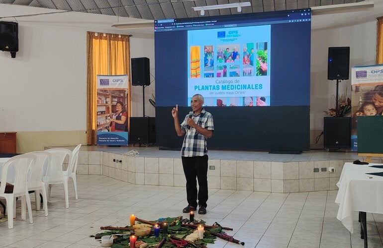 Un hombre frente a una pantalla luminosa, presenta el catálogo de plantas medicinales del pueblo maya Ch'orti'