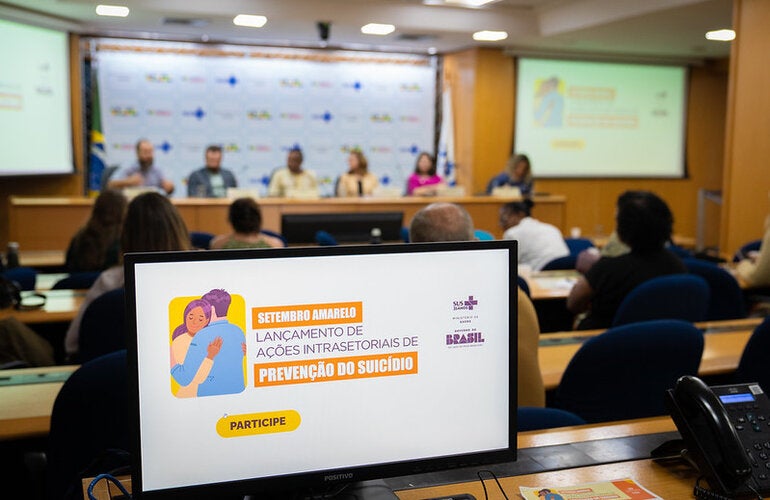 logomarca do evento, ao fundo mesa de palestrantes