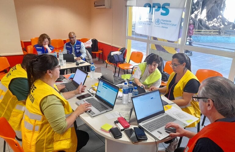 participantes de taller con chalecos amarillos, sentados alrededor de una mesa con laptops